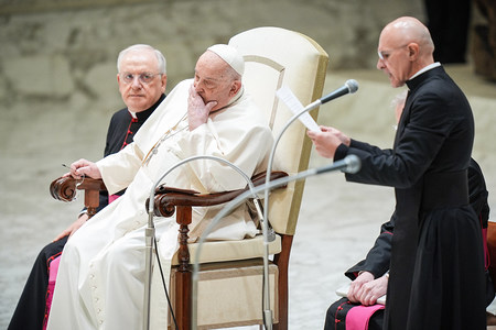 Papst Franziskus hält sich die Hand vor den Mund, da er an Bronchitis erkrankt ist, Pater Pierluigi Giroli (r.) spricht, bei der Generalaudienz am 12. Februar 2025 im Vatikan.