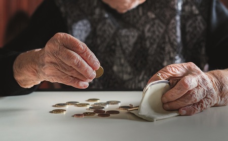 Elderly 95 years old woman sitting miserably at the table at home and counting remaining coins from the pension in her wallet after paying the bills.
