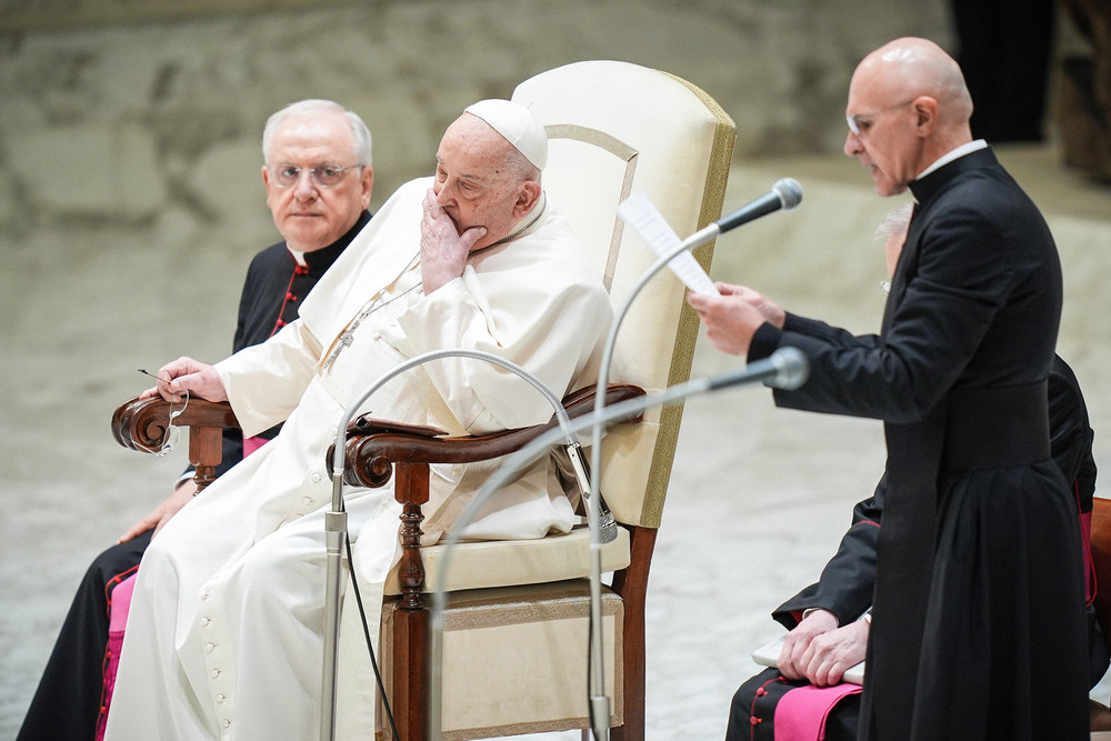 Audienz mit Papst Franziskus / Copyright 2025, KNA GmbH, www.kna.de, All Rights Reserved, Lola Gomez Papst Franziskus hält sich die Hand vor den Mund, da er an Bronchitis erkrankt ist, Pater Pierluigi Giroli (r.) spricht, bei der Generalaudienz am 12. Februar 2025 im Vatikan.